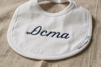 Bavoir bébé personnalisé en coton bio avec broderie prénom et label Made in France, posé sur du lin naturel